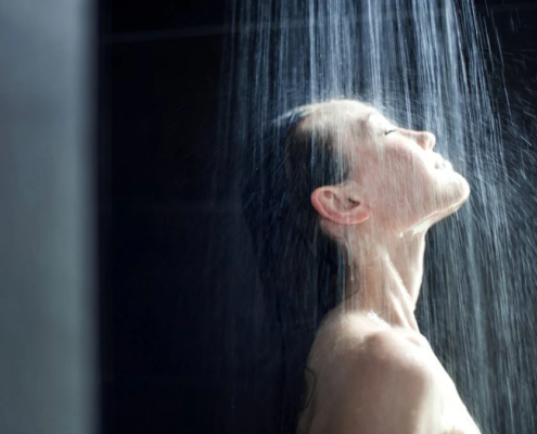 Mulher tomando banho com água caindo sobre o rosto em ambiente escuro