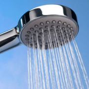 Chuveiro cromado com água saindo contra fundo azul