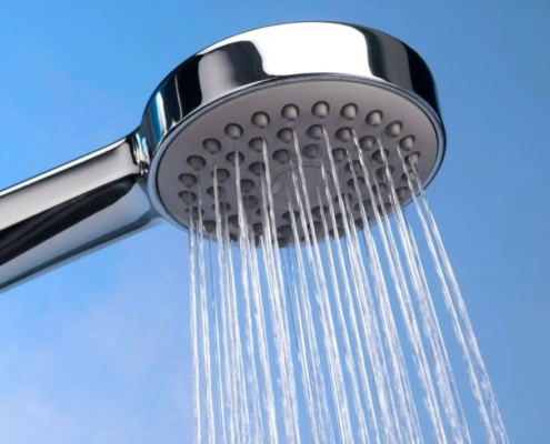 Chuveiro cromado com água saindo contra fundo azul