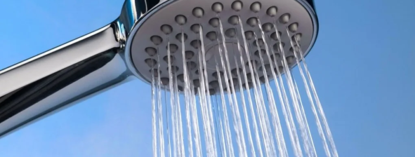 Chuveiro cromado com água saindo contra fundo azul