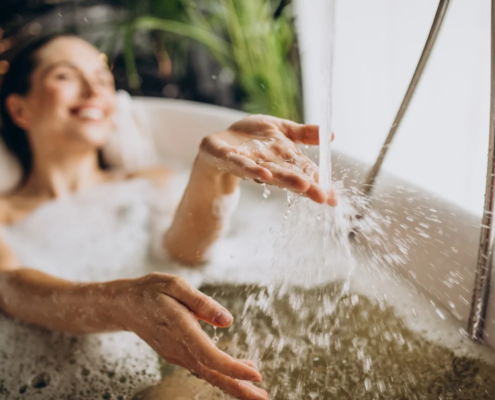 Mulher relaxando em banheira com espuma enquanto água cai sobre as mãos