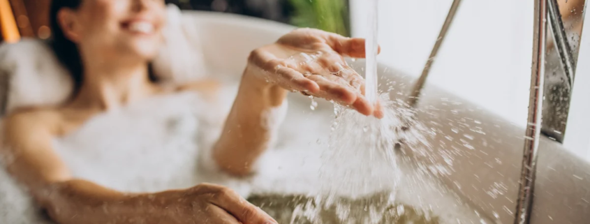 Mulher relaxando em banheira com espuma enquanto água cai sobre as mãos