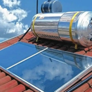 Sistema de aquecimento solar instalado em telhado de casa, com painel solar e cilindro de armazenamento, aproveitando energia solar para aquecimento de água.