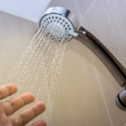 Mão sob chuveiro com água corrente em banheiro moderno