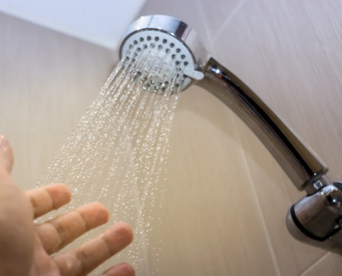 Mão sob chuveiro com água corrente em banheiro moderno