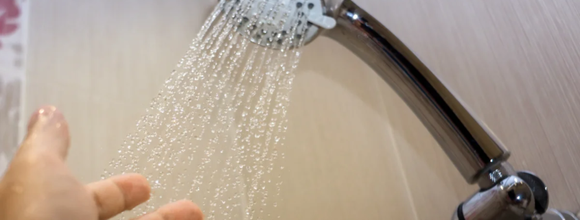 Mão sob chuveiro com água corrente em banheiro moderno