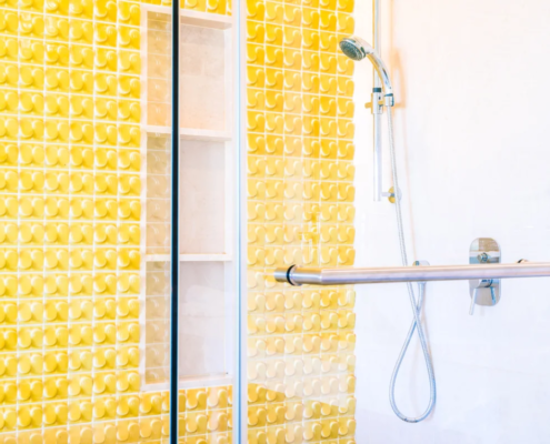 Banheiro moderno com azulejos amarelos texturizados e box de vidro com chuveiro de mão cromado