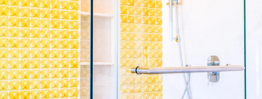 Banheiro moderno com azulejos amarelos texturizados e box de vidro com chuveiro de mão cromado